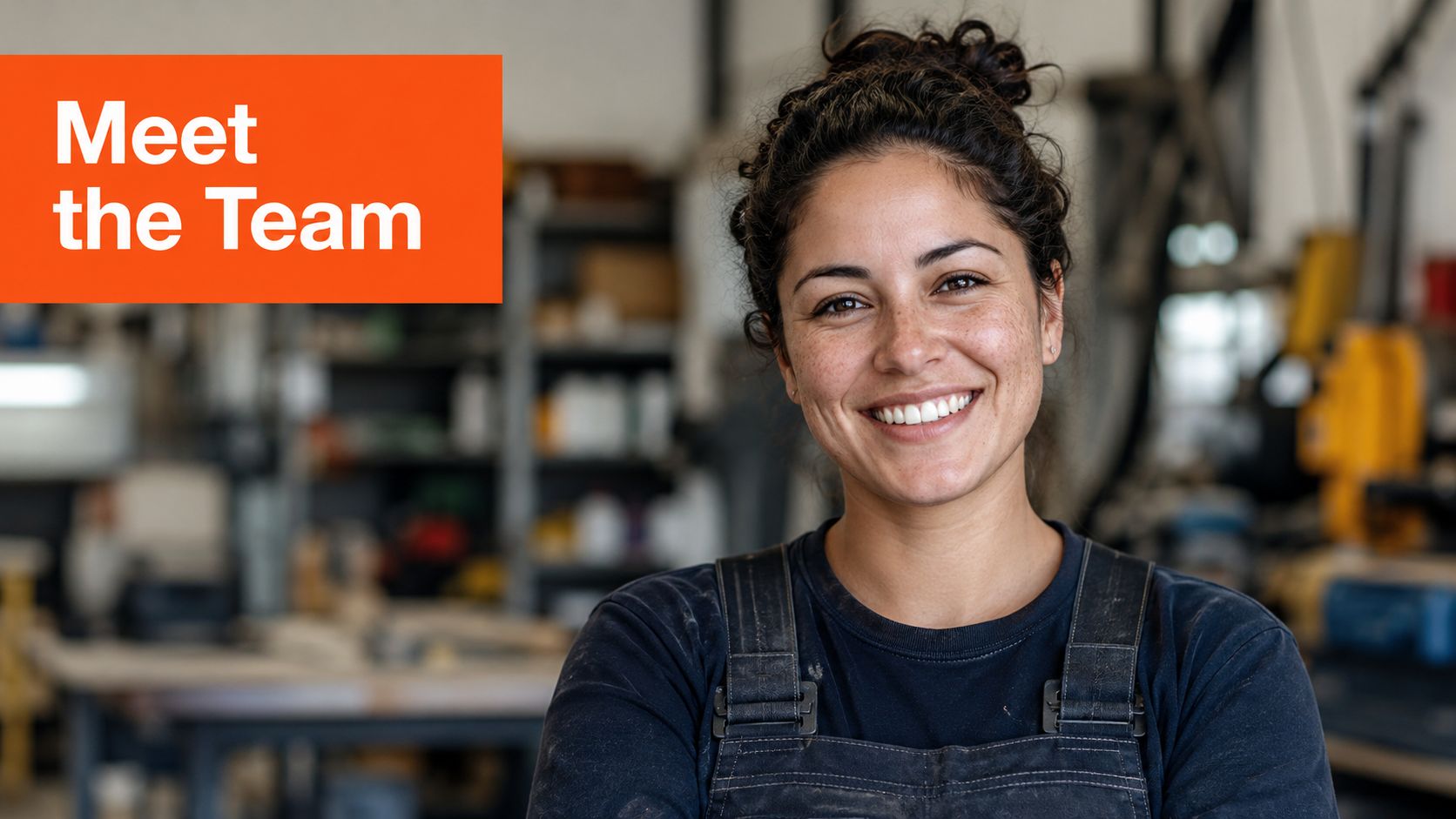 A smiling woman in work overalls posing in a professional workshop, representing behind the scenes team.