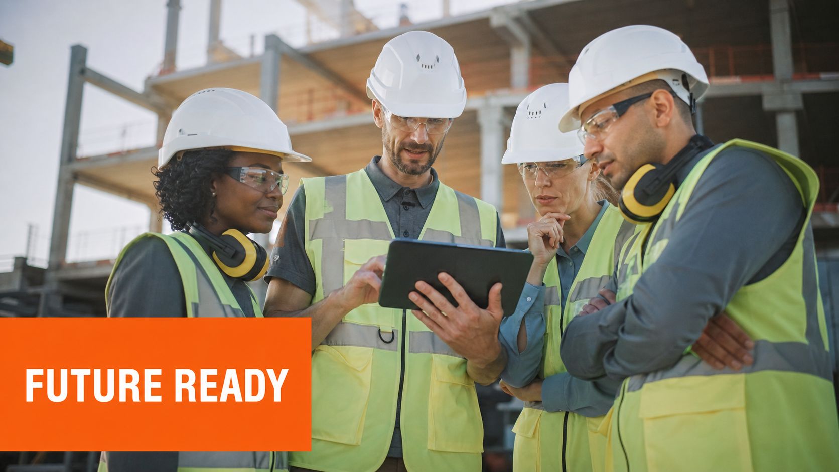 A diverse team of professional engineers in hard hats reviewing project plans on a digital tablet at construction site.